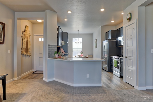 kitchen with a peninsula, appliances with stainless steel finishes, light countertops, and a chandelier