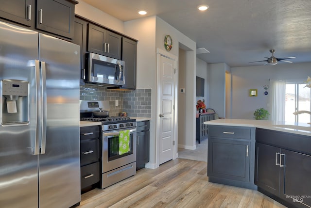 kitchen featuring light wood-style flooring, a sink, light countertops, appliances with stainless steel finishes, and decorative backsplash