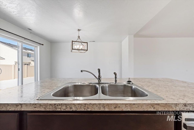 kitchen featuring sink, hanging light fixtures, an island with sink, a textured ceiling, and a chandelier