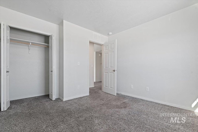 unfurnished bedroom with a closet, a textured ceiling, and dark colored carpet