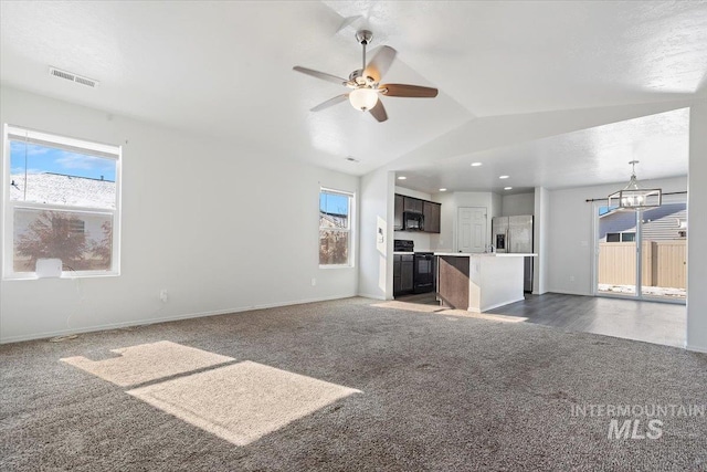 unfurnished living room with plenty of natural light, vaulted ceiling, and dark colored carpet