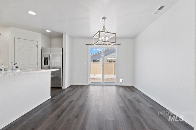 unfurnished dining area with dark hardwood / wood-style flooring, sink, a textured ceiling, and an inviting chandelier