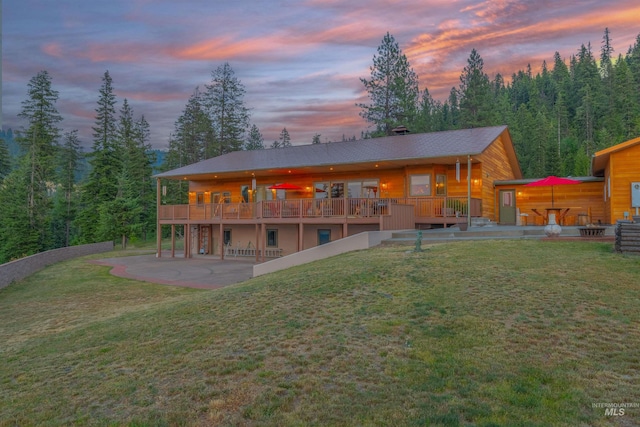 back of house at dusk with a patio, a yard, and a deck