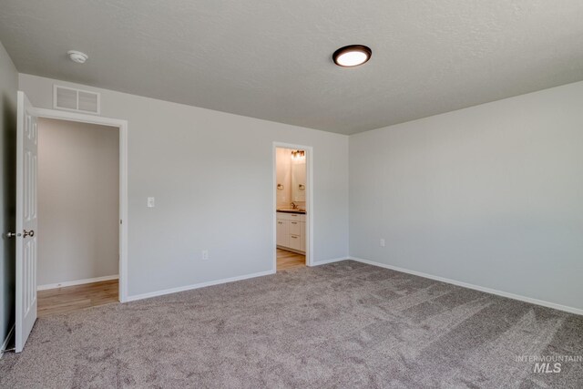 7417 E Shields Dr, Nampa, ID 83687 - unfurnished bedroom featuring visible vents, a textured ceiling, ensuite bath, baseboards, and light colored carpet
