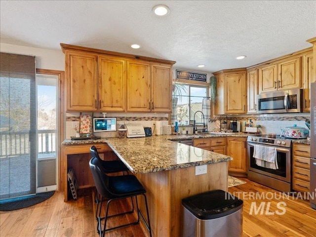 kitchen with light hardwood / wood-style flooring, backsplash, stainless steel appliances, light stone countertops, and a kitchen bar