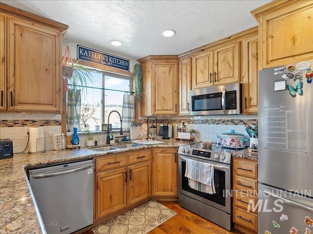 kitchen with stainless steel appliances, light stone countertops, sink, and decorative backsplash