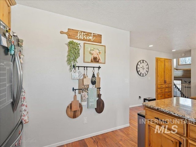 kitchen with stainless steel refrigerator, a textured ceiling, light stone counters, and light hardwood / wood-style flooring