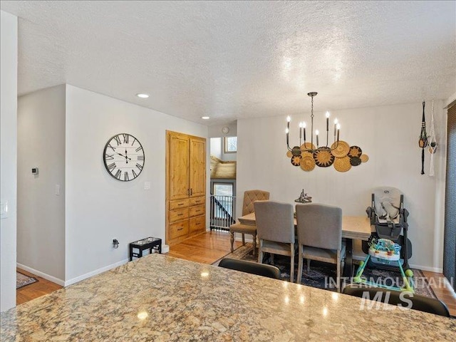 dining space with a notable chandelier, a textured ceiling, and light wood-type flooring