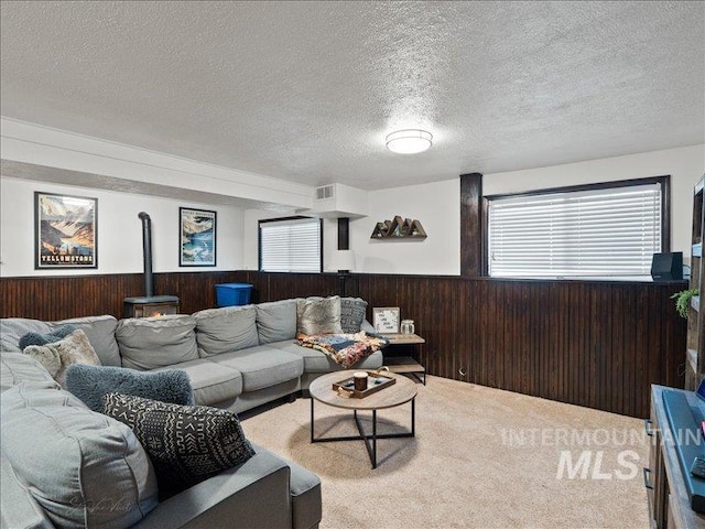 carpeted living room with a wood stove, a textured ceiling, and wooden walls