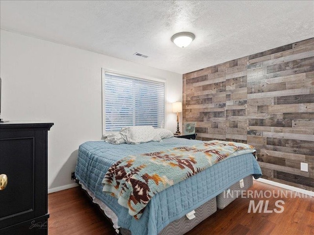 bedroom with dark hardwood / wood-style flooring, a textured ceiling, and wooden walls