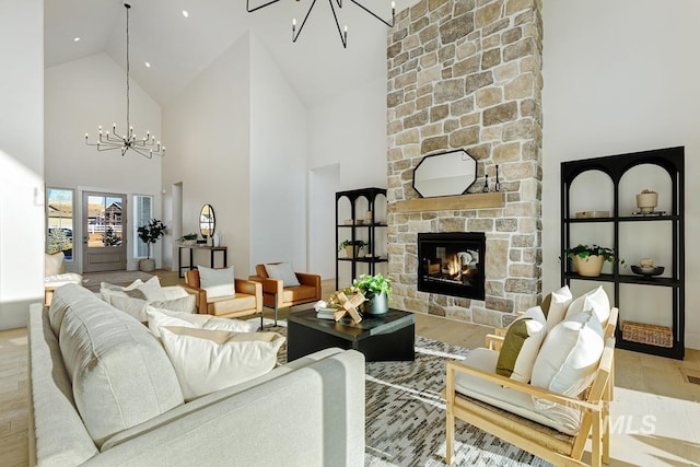 living room featuring high vaulted ceiling, wood finished floors, a notable chandelier, and a stone fireplace