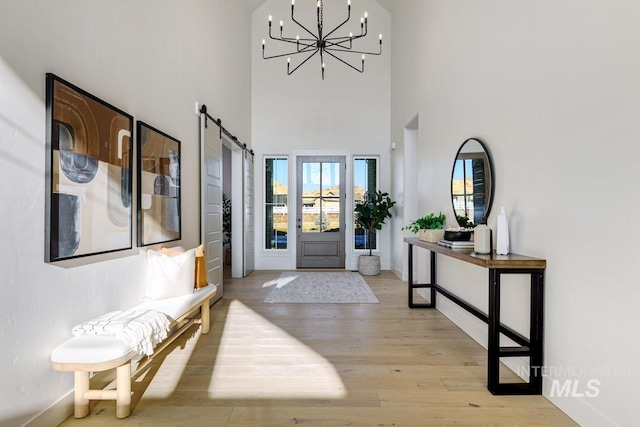 foyer with light wood-style floors, an inviting chandelier, baseboards, and a barn door