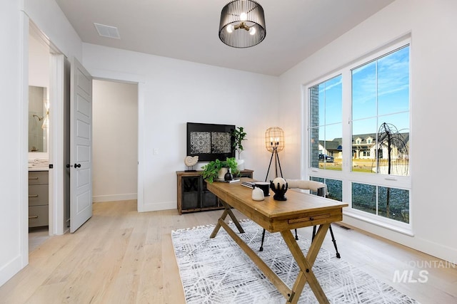 office area with light wood-style floors, visible vents, and baseboards