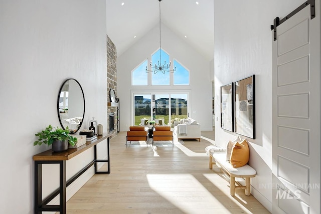 sitting room featuring a fireplace, a barn door, an inviting chandelier, high vaulted ceiling, and light wood-type flooring