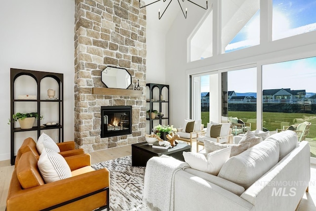 living room featuring an inviting chandelier, a stone fireplace, a towering ceiling, and wood finished floors