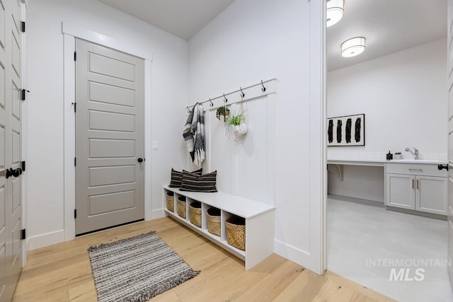 mudroom with light wood-type flooring, a sink, and baseboards