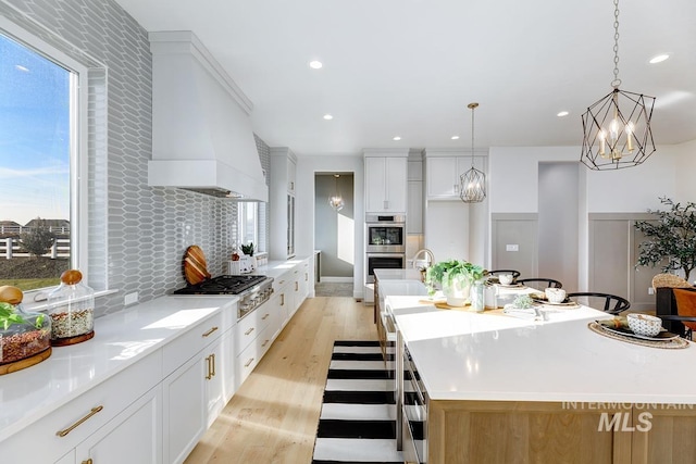 kitchen featuring backsplash, appliances with stainless steel finishes, white cabinets, light wood-type flooring, and a large island with sink