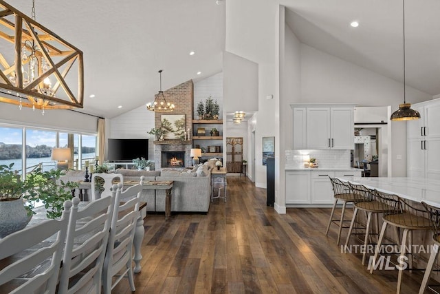 interior space with a chandelier, high vaulted ceiling, dark wood-style flooring, and a brick fireplace