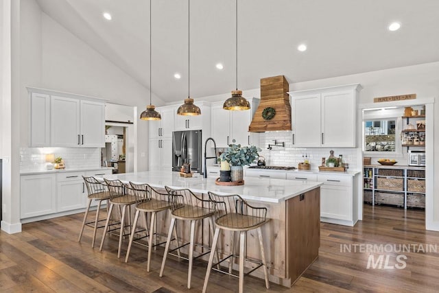 kitchen with premium range hood, refrigerator with ice dispenser, gas stovetop, and white cabinetry