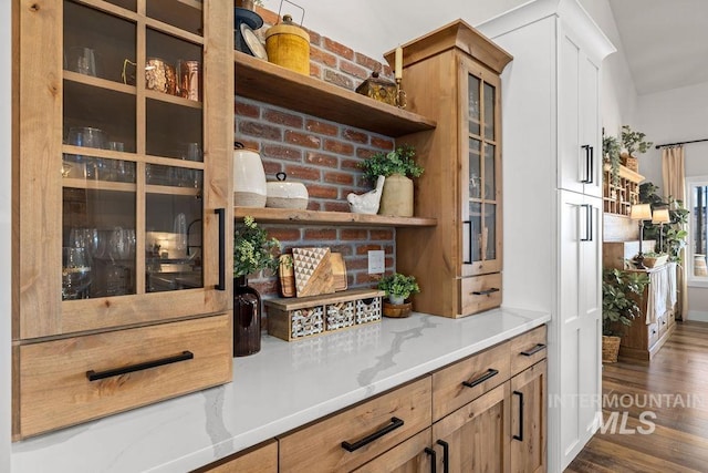 interior space featuring light stone counters, glass insert cabinets, open shelves, and dark wood-style flooring