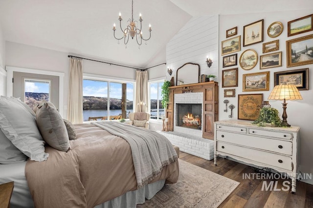 bedroom with high vaulted ceiling, a notable chandelier, dark wood-type flooring, a water view, and a fireplace