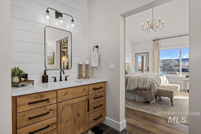 ensuite bathroom with baseboards, connected bathroom, wood finished floors, vanity, and a chandelier