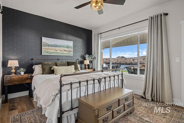 bedroom featuring a ceiling fan, baseboards, brick wall, and wood finished floors