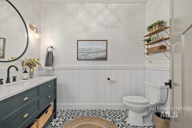 half bath with toilet, tile patterned floors, vanity, and wainscoting