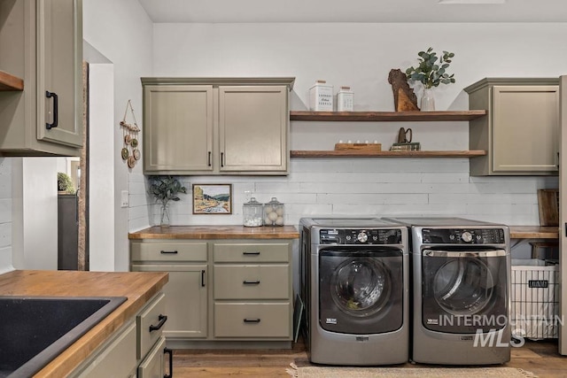 clothes washing area with a sink, cabinet space, washer and clothes dryer, and wood finished floors