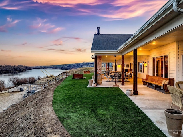 yard at dusk with a patio area and a water view