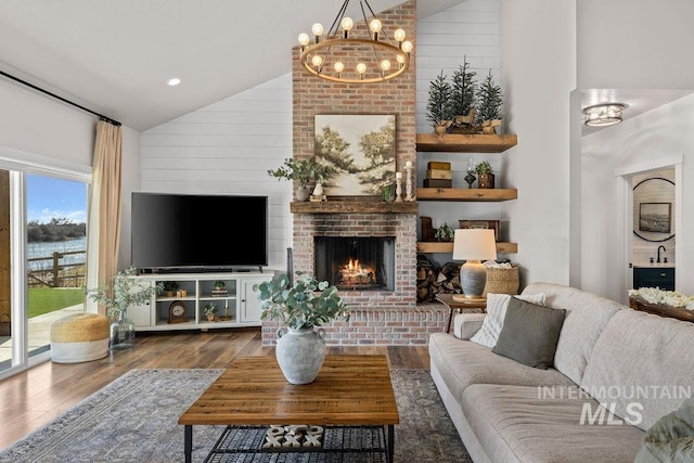 living area featuring high vaulted ceiling, a brick fireplace, an inviting chandelier, and wood finished floors