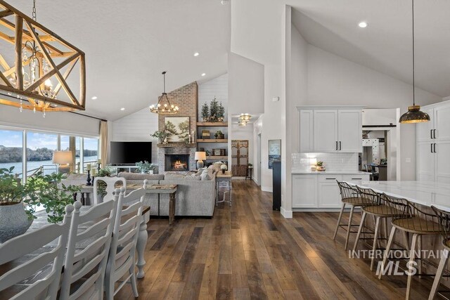 interior space with a notable chandelier, a fireplace, high vaulted ceiling, and dark wood-type flooring