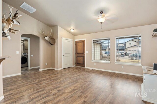 unfurnished living room with visible vents, lofted ceiling, washer / dryer, wood finished floors, and arched walkways