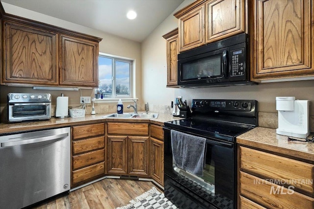 kitchen featuring a sink, black appliances, wood finished floors, and light countertops