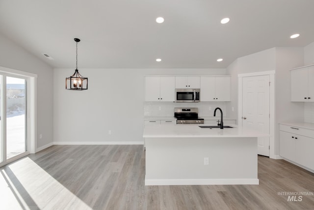 kitchen featuring an island with sink, hanging light fixtures, sink, white cabinetry, and stainless steel appliances