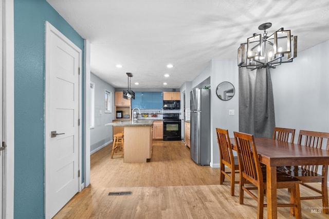 kitchen with a breakfast bar area, a kitchen island with sink, black appliances, decorative light fixtures, and light wood-type flooring