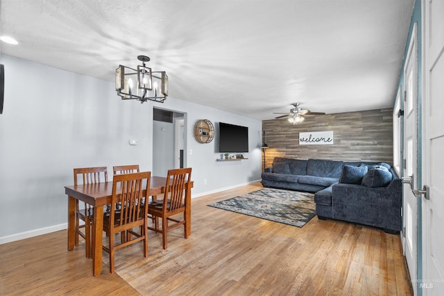 dining area with ceiling fan with notable chandelier, hardwood / wood-style floors, and wooden walls