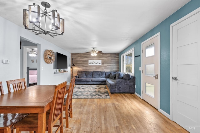 dining space featuring ceiling fan with notable chandelier, light hardwood / wood-style flooring, and wood walls