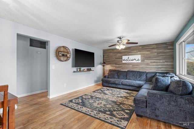 living room featuring ceiling fan, light hardwood / wood-style flooring, and wood walls