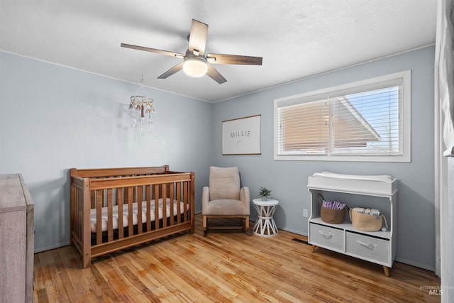 bedroom with a crib, ceiling fan, and light hardwood / wood-style flooring