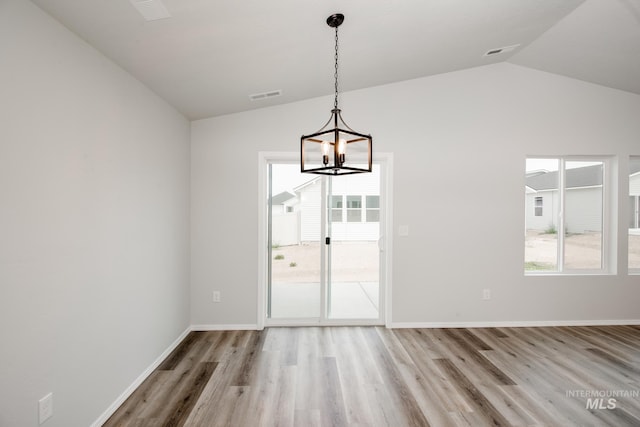 unfurnished dining area featuring lofted ceiling, a healthy amount of sunlight, a chandelier, and light hardwood / wood-style flooring