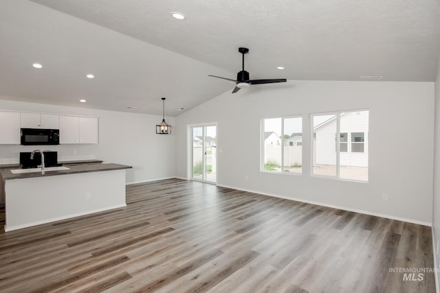 unfurnished living room with ceiling fan, wood finished floors, a sink, baseboards, and vaulted ceiling