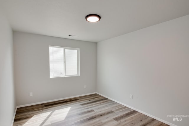 spare room featuring light wood-type flooring, visible vents, and baseboards