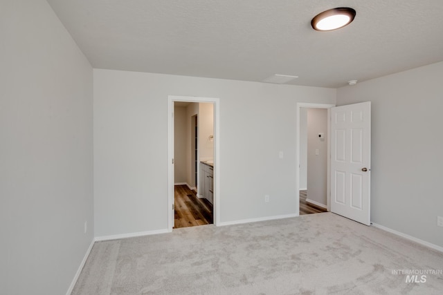 unfurnished bedroom with ensuite bath, carpet, baseboards, and a textured ceiling