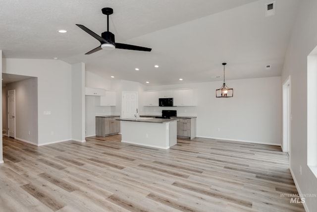 interior space featuring lofted ceiling, ceiling fan, white cabinets, a center island with sink, and decorative light fixtures