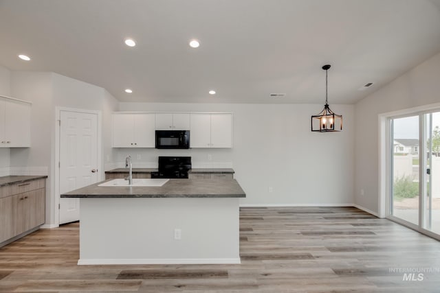 kitchen featuring pendant lighting, an island with sink, sink, white cabinets, and range