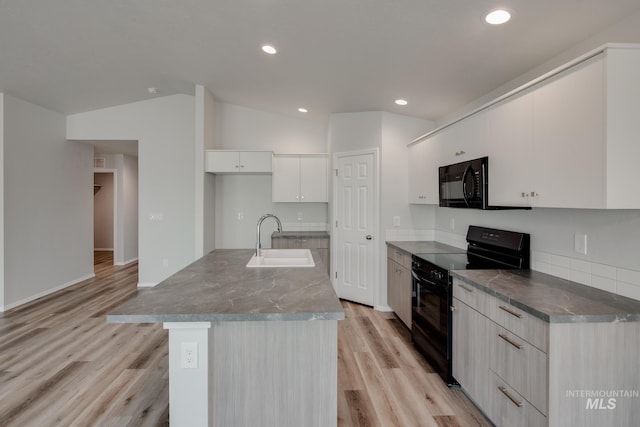 kitchen with vaulted ceiling, an island with sink, sink, white cabinets, and black appliances