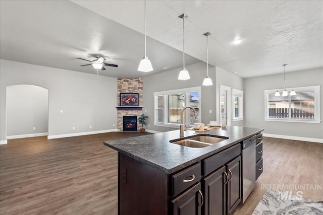 kitchen with dark wood-style floors, arched walkways, a sink, a stone fireplace, and dishwasher