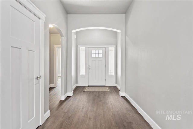 foyer featuring arched walkways, dark wood finished floors, and baseboards