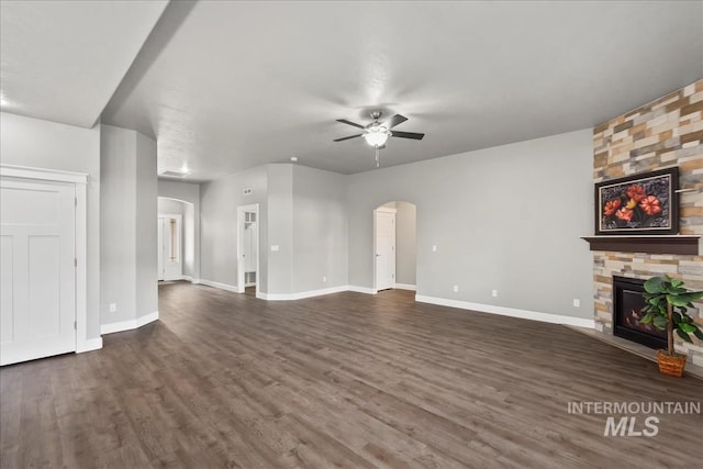 unfurnished living room featuring arched walkways, a fireplace, dark wood finished floors, and baseboards